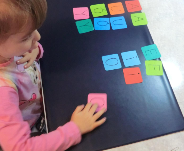 Dziecko czyta samogłoski na kolorowych karteczkach